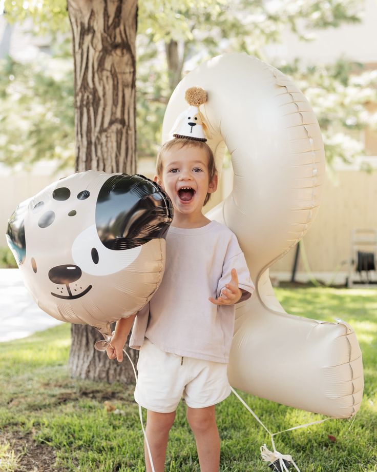 a little boy holding two balloons in the shape of a dog and a cow head