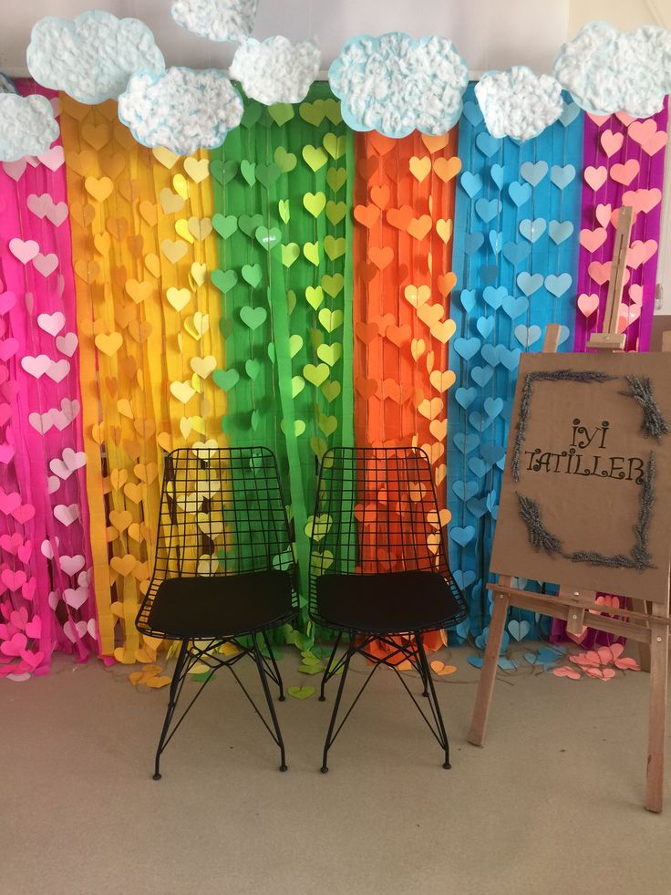 two chairs are sitting in front of a rainbow backdrop with hearts and clouds on it