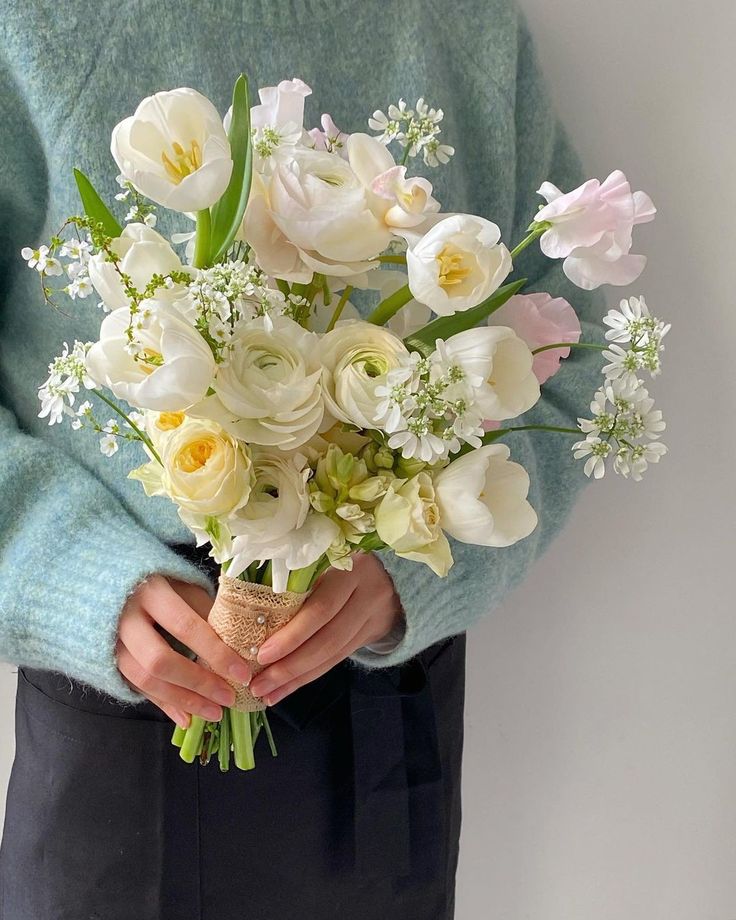 a person holding a bouquet of white flowers in their hands and wearing a blue sweater