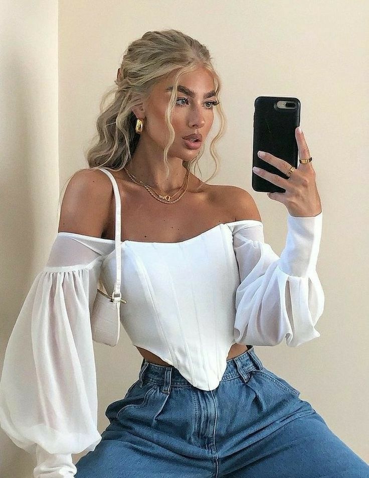 a woman taking a selfie while sitting on a bed wearing jeans and a white top