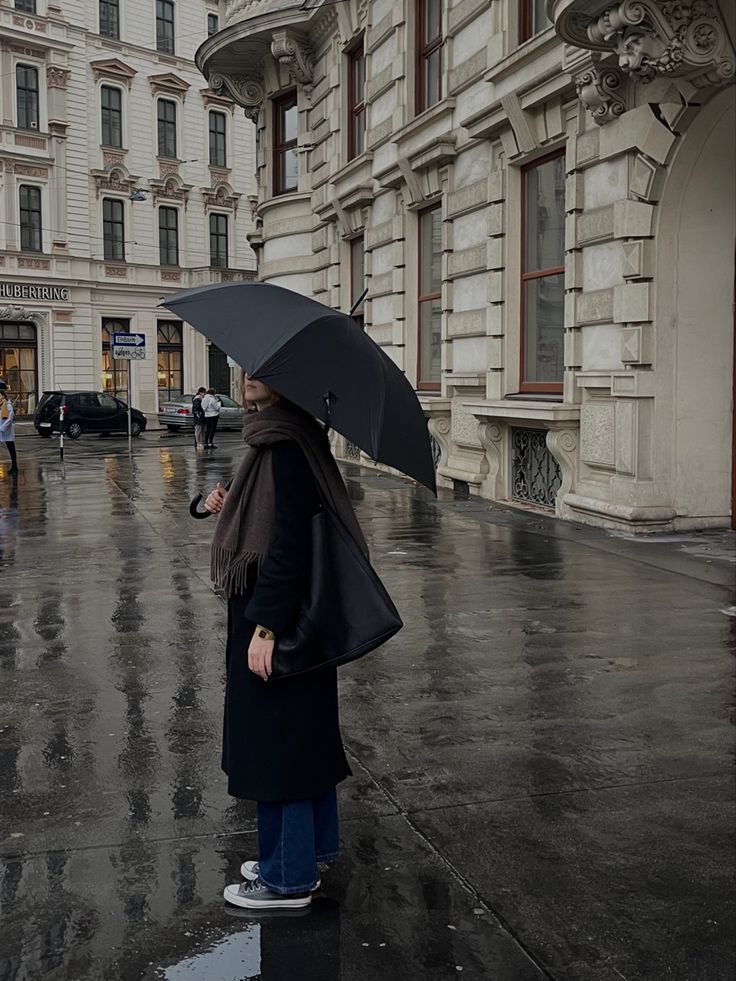 a woman standing in the rain holding an umbrella