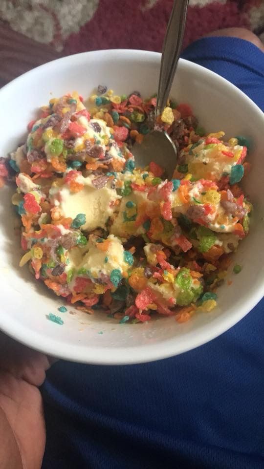 a person is holding a bowl full of cereal and ice cream with a spoon in it