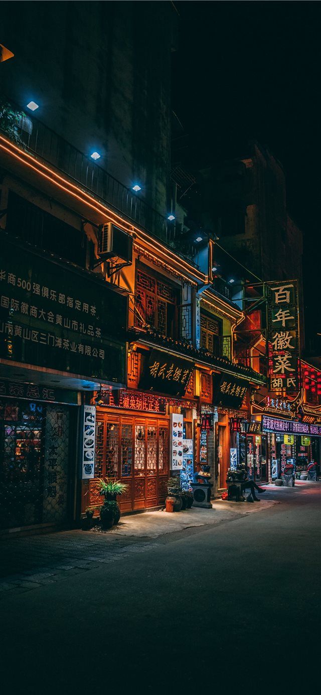 an empty street at night with neon signs on the buildings and lights in the dark