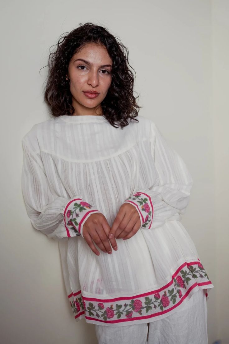 A white self stripes textile gathered top with hand block printed Gulabi at the hem and cuff This timeless and versatile top will be a staple in your warm-weather wardrobe. Spring White Blouse With Block Print, White Spring Blouse With Smocked Cuffs, Traditional White Tops With Block Print, White Traditional Block Print Tops, Bohemian White Blouse With Embroidered Cuffs, Traditional White Block Print Top, White Peasant Top With Smocked Cuffs And Long Sleeves, White Long Sleeve Blouse With Smocked Cuffs, White Bohemian Blouse With Embroidered Cuffs