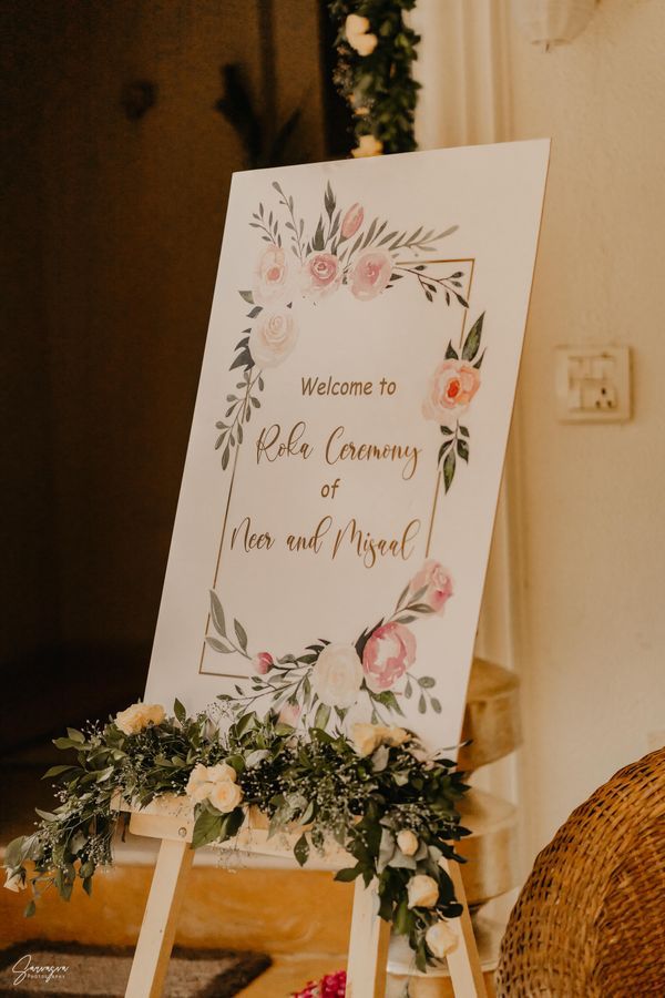 a welcome sign sitting on top of a wooden easel next to flowers and greenery