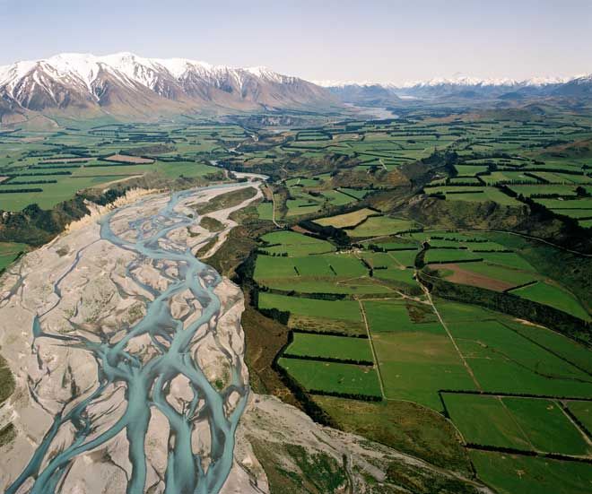 an aerial view of a river running through a valley with mountains in the back ground