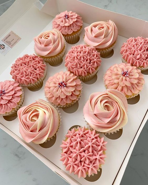 twelve cupcakes with pink frosting in a box on a marble countertop