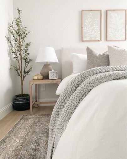 a bed with white sheets and pillows next to a lamp on a wooden table in a bedroom