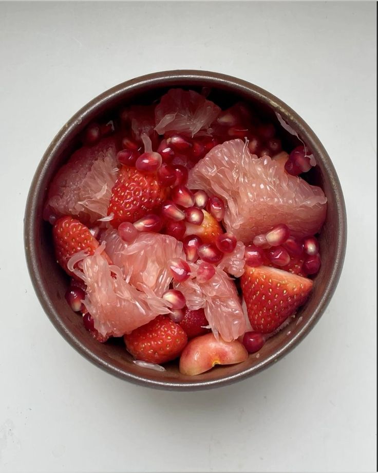 a bowl filled with fruit and pomegranates on top of a table