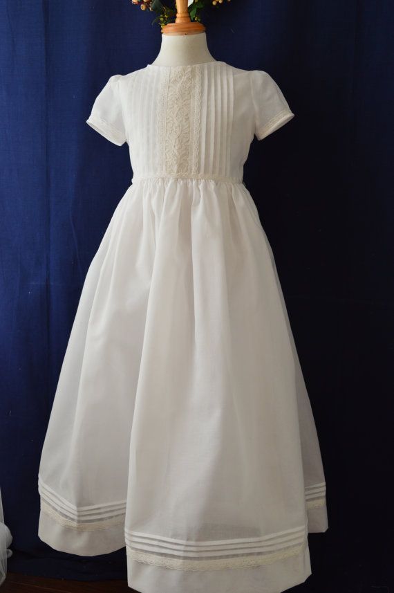 Maria   Classic communion dress beautifully hand crafted with fine swiss cotton. Simple yet elegant with hues of ivory and white. Exquisite embellishment of fine hand embroidered shadow work.  The center bodice of this georgeous communion dress is decorated with hand embroidered ivory organza silk and framed with delicate bobbin lace and rows of fine tucks. Front bodice joint trimmed with bobbin lace. Short sleeves with pinch of puff trimmed with delicate bobbin lace and piping. Generously ga... First Communion Gown With Lace Trim And Fitted Bodice, Elegant First Communion Dress With Lace Collar, Classic Lace Dress For First Communion, Classic Lace Work Dress For First Communion, Cream Scalloped Lace Dress For First Communion, Classic First Communion Dress With Lace Trim For Baptism, Classic First Communion Dress With Lace Trim, First Communion Dress With Lace Trim, Elegant First Communion Dress With Lace Work For Confirmation