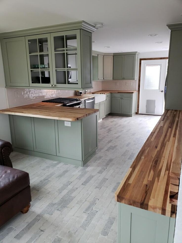 an empty kitchen with green cabinets and wooden counter tops, along with a brown leather couch