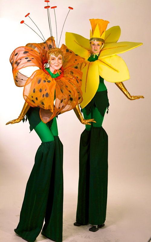 two women dressed in green and yellow are holding large paper flower shaped kites on their heads