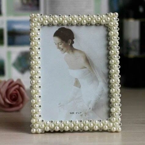 a white photo frame with pearls around it on a table next to a pink rose