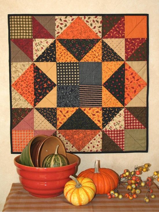 a table topped with a red bowl filled with pumpkins next to a wall hanging