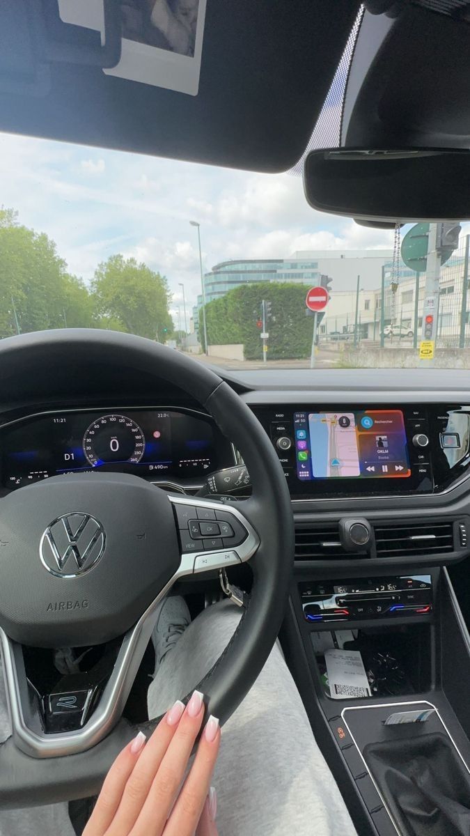 a woman driving a car with her hand on the steering wheel while holding onto an electronic device