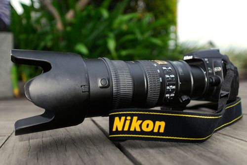 a black and white photo of a nikon camera on a wooden table with plants in the background