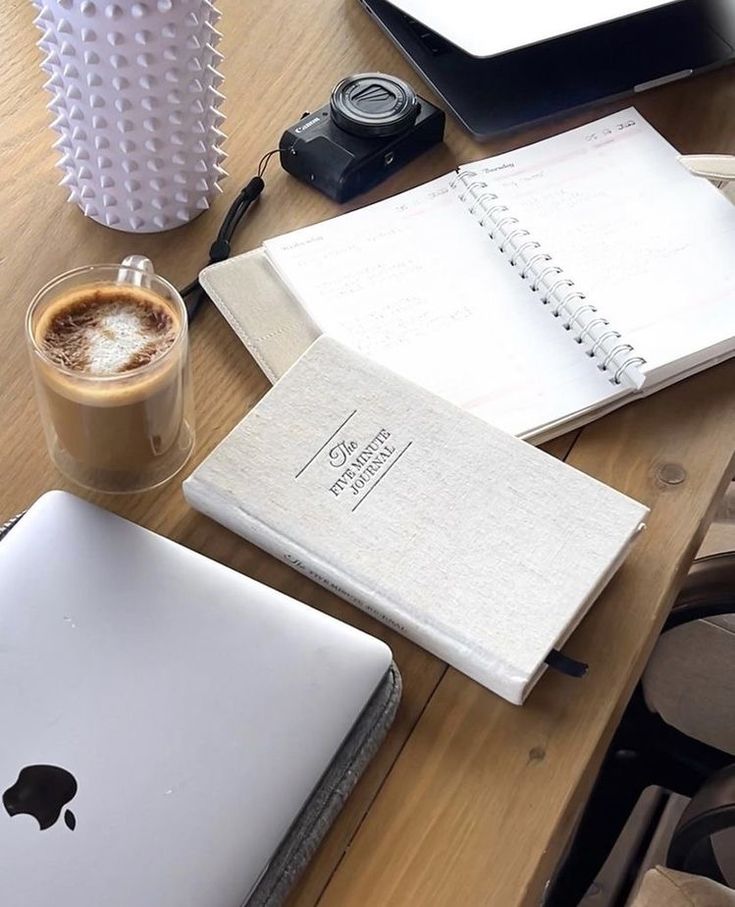 an apple laptop computer sitting on top of a wooden desk next to a cup of coffee