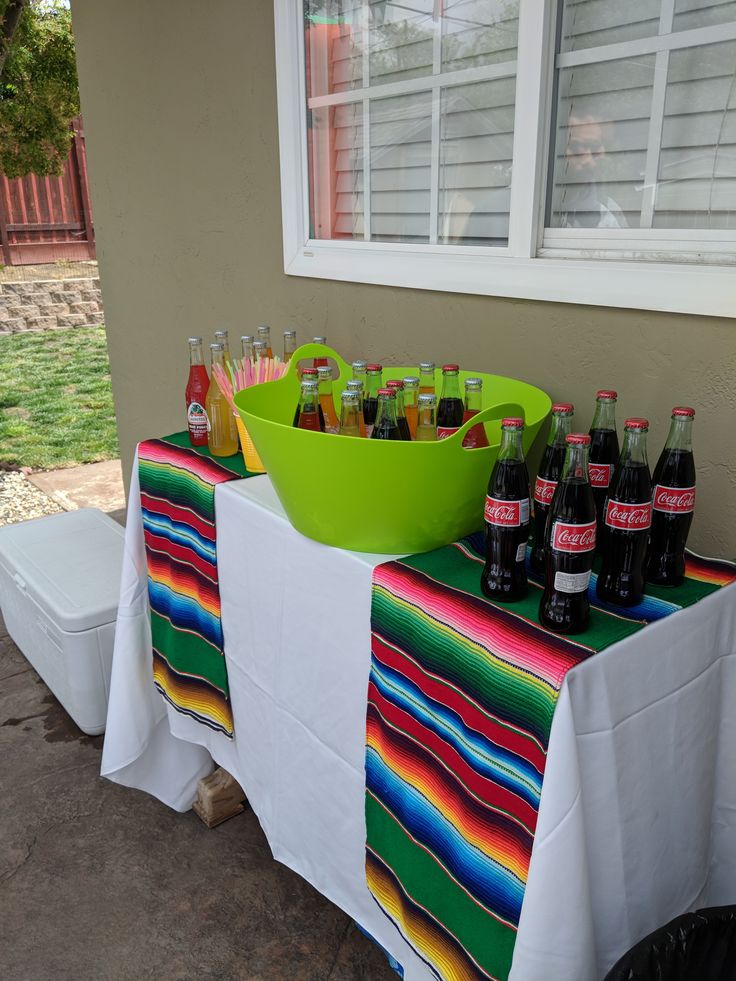 a table topped with bottles of beer next to a green bowl on top of a white table cloth