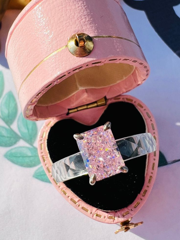 an open pink box with a ring in it's center and some glitter on the inside