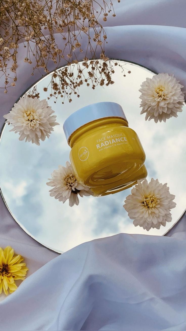 a jar of honey sitting on top of a mirror next to flowers and blue fabric