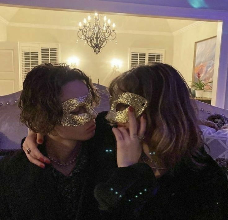 two women wearing gold glitter masks in a living room with chandelier above them