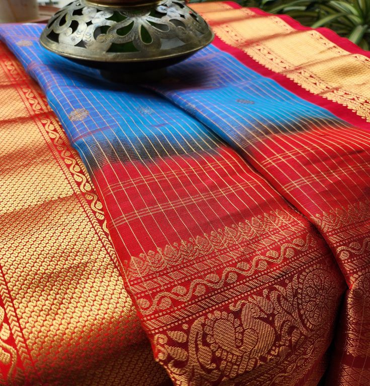 Interwoven borders in bright colors, make this saree ideal for a wedding function. Checks with Peacock as motifs on Aanchal and Bootis all over Weave: Handloom Gadwal Fabric: Pure silk Length: 5.5mts + Blouse piece Color: Dual tone Blue and Red Multicolor Pre-draped Saree With Zari Weaving, Multicolor Pre-draped Saree With Zari Work For Puja, Multicolor Pre-draped Saree With Zari Weaving For Festive, Festive Multicolor Tissue Silk Pre-draped Saree, Navratri Saree For Rituals With Pallu Detail, Semi-stitched Pallu Saree For Rituals, Multicolor Chanderi Pre-draped Saree For Traditional Ceremonies, Zari Weaving Lehenga For Rituals And Festivals, Navratri Saree With Zari Weaving For Rituals