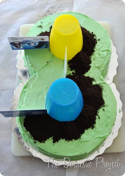 a cake with green frosting and dirt on it, being cut by a knife