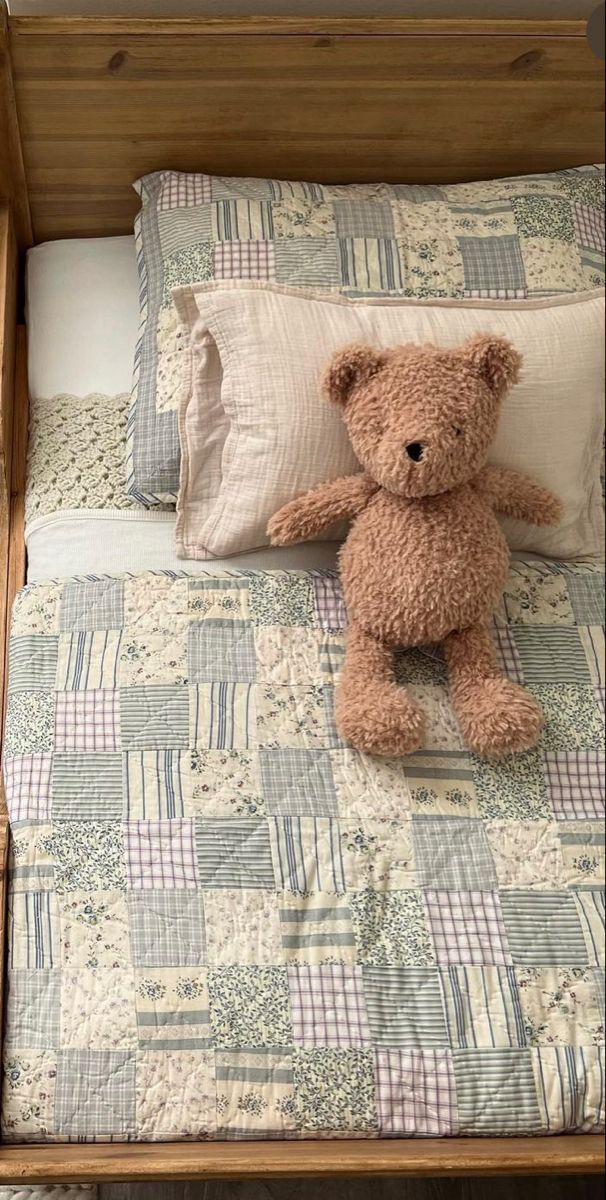 a brown teddy bear sitting on top of a bed next to pillows and pillow cases