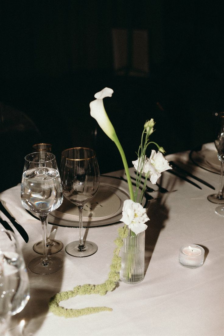 A chic wedding table decor of calla lilies and delicate white blooms against dark table settings. Lilies Wedding Centerpieces, Lily Wedding Centerpieces Simple, Calla Lily Arch Wedding, Calalilies Flowers, White Calla Lily Centerpiece, Calla Lillies Centerpieces Wedding, Calla Lily Orchid Bouquet, White Tulips Wedding Decoration, Cala Lillies Bride Bouquet