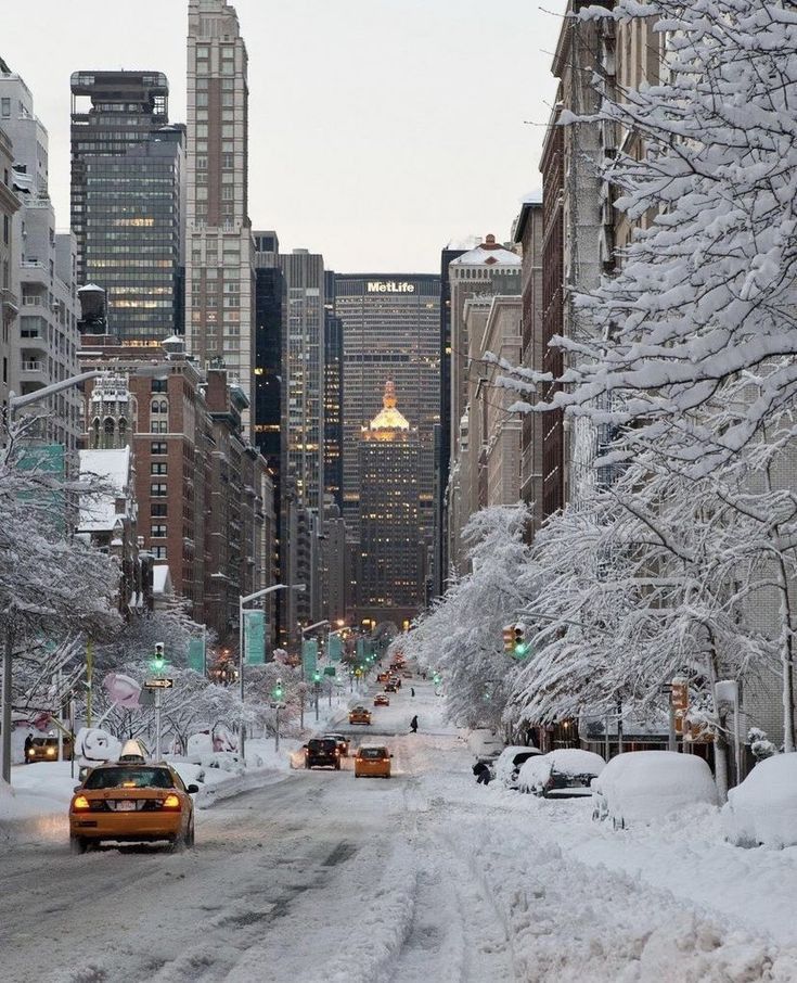 cars driving down a snow covered street in the middle of tall buildings and skyscrapers