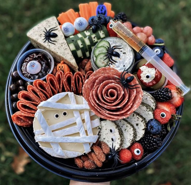 a hand holding a halloween platter with cheese, crackers and other food items