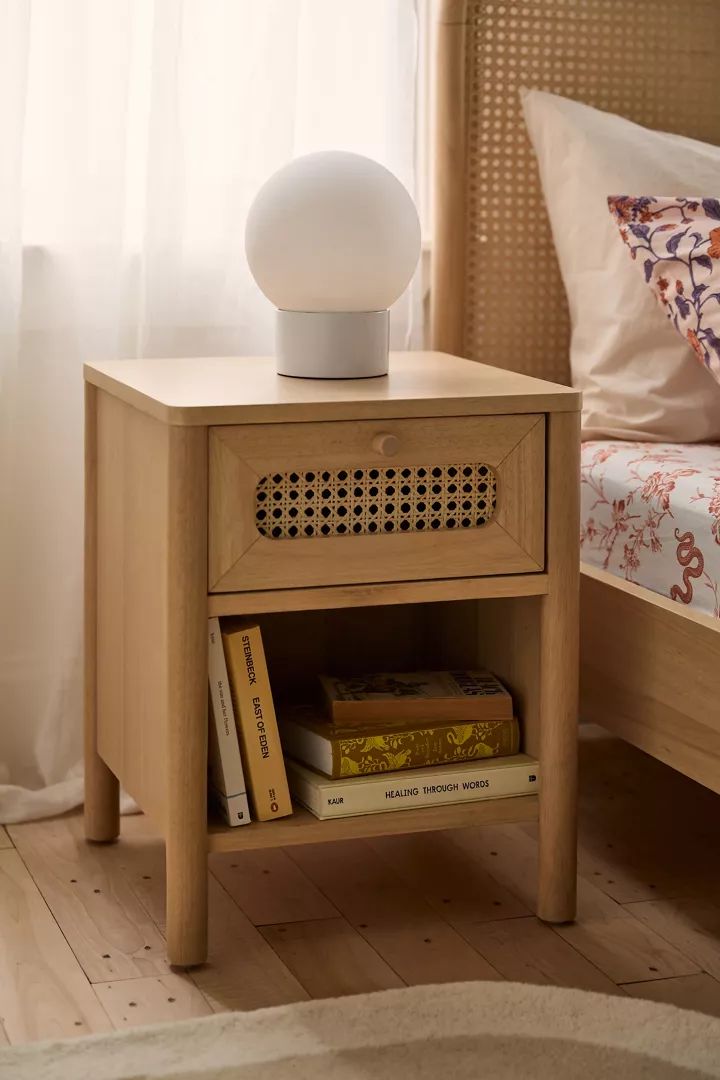 a nightstand with a lamp on top of it next to a bed