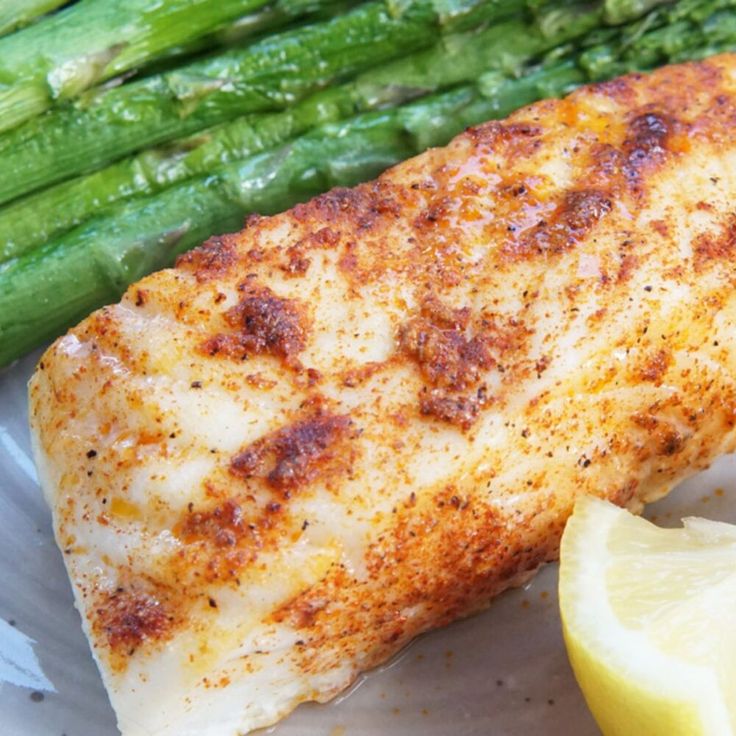 a piece of fish and asparagus on a plate with lemon wedges next to it