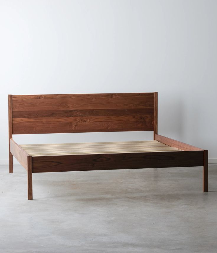 a bed with wooden headboard and foot board on concrete flooring next to white wall