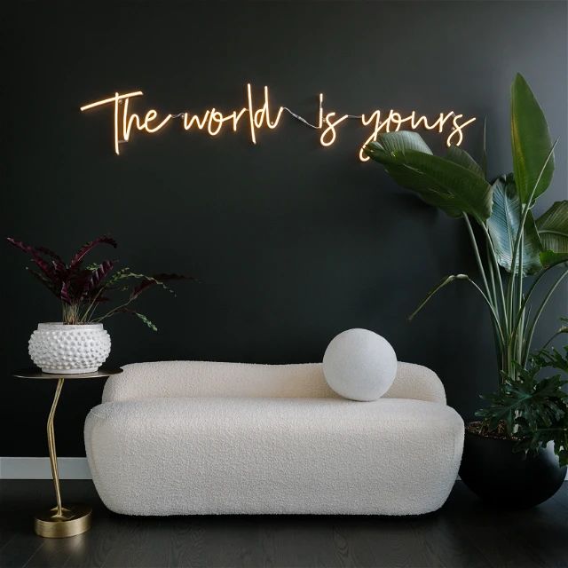 the world is yours neon sign in front of a white couch and potted plant