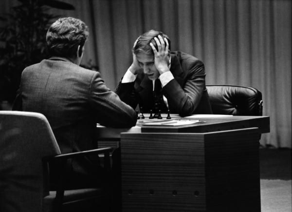 two men are sitting at a table with their heads in their hands and one is holding his hand to his head