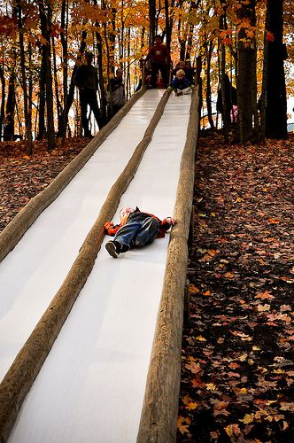 a person laying on the ground next to a long slide in the middle of trees