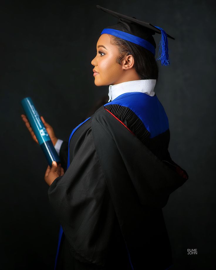 a woman in a graduation gown holding a blue book and looking off into the distance