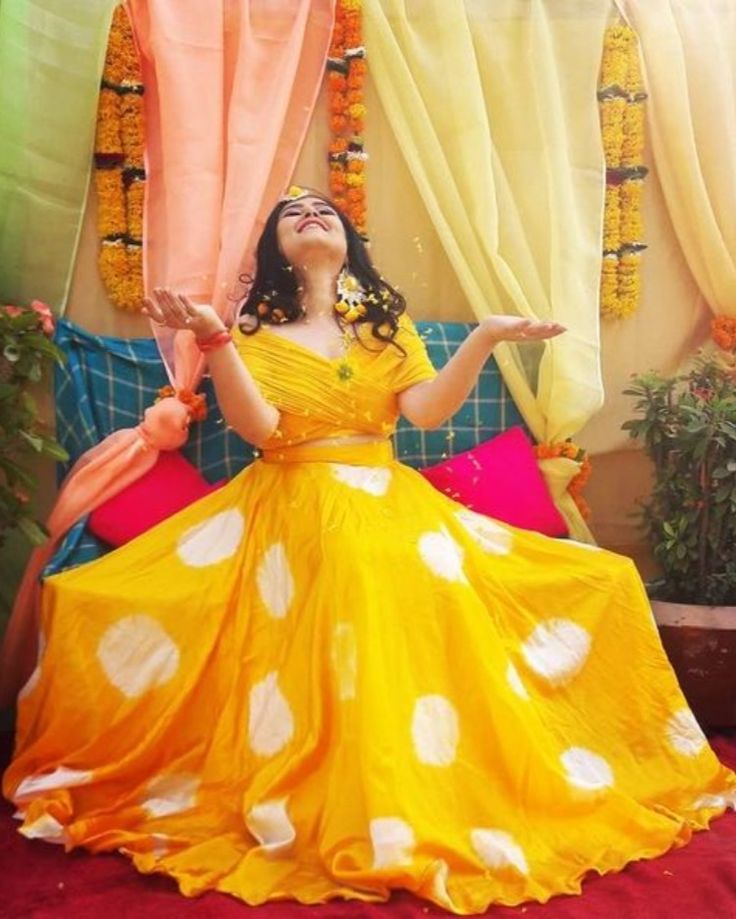 a woman in a yellow and white dress sitting on a couch with her hands up