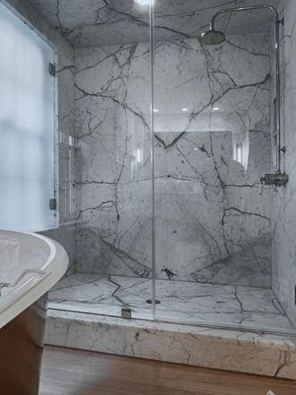 a bathroom with marbled walls and flooring next to a bathtub in the corner