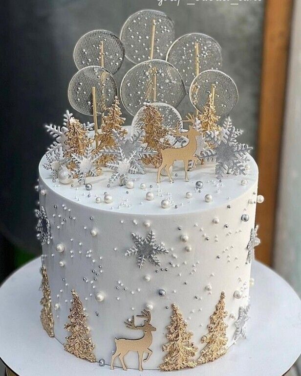 a white and gold christmas cake decorated with trees, snowflakes and reindeers