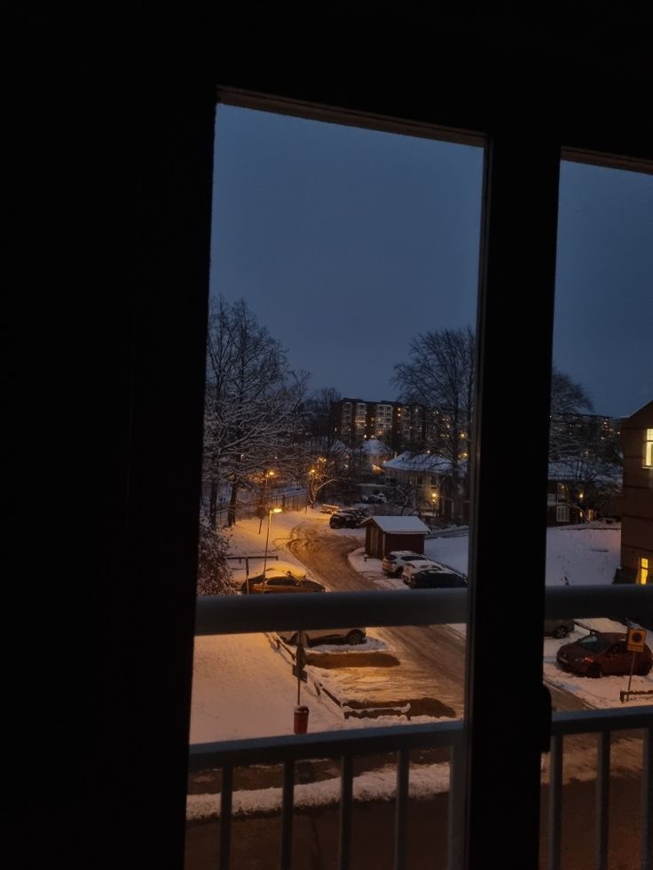 the view from an apartment window at night with snow on the ground and buildings in the distance