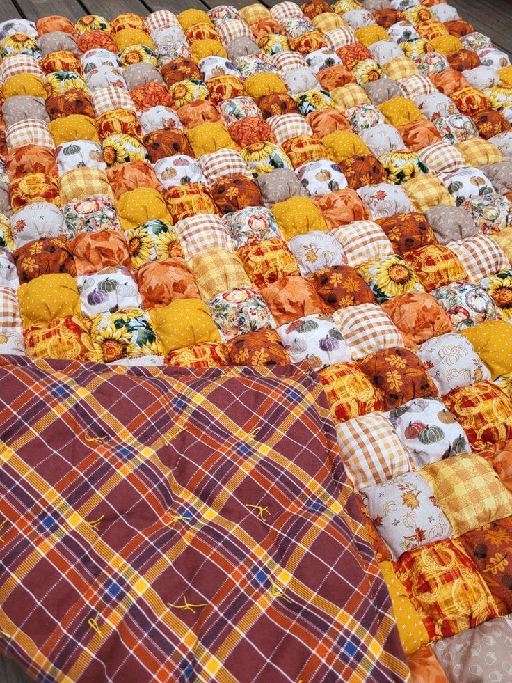 an orange and yellow quilt is laying on a wooden table top with plaid fabric around it