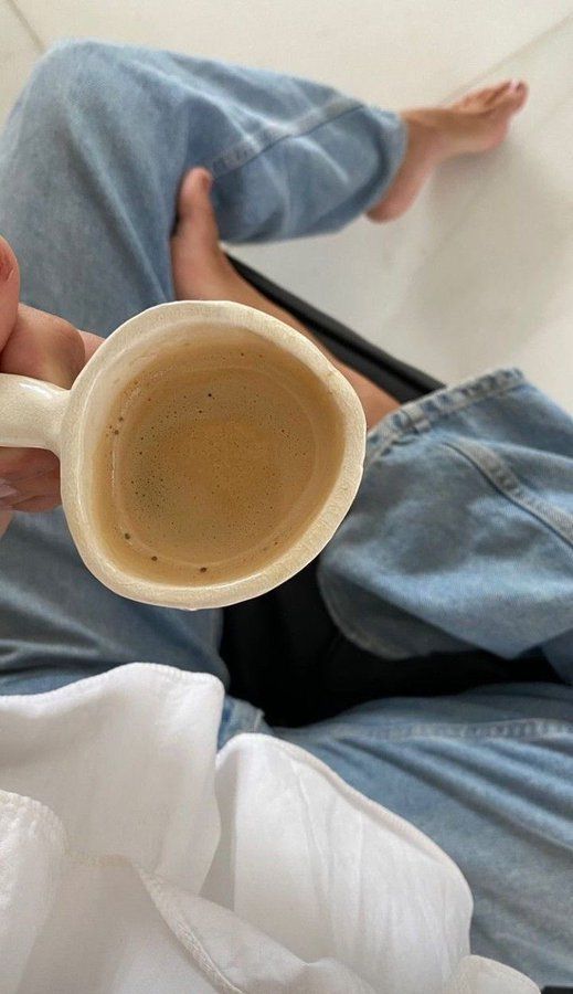 a person sitting on the floor holding a coffee cup in their hand with both hands