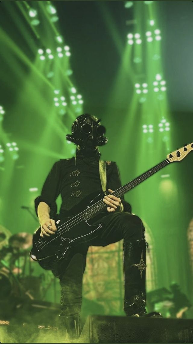 a man in a black outfit playing a guitar on stage with green lights behind him