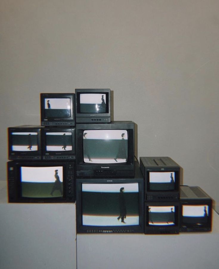 several televisions stacked on top of each other in front of a wall with one person standing between them