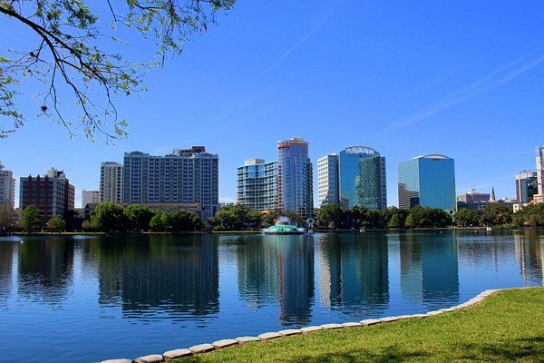 a lake with buildings in the background and grass on the bank next to it,