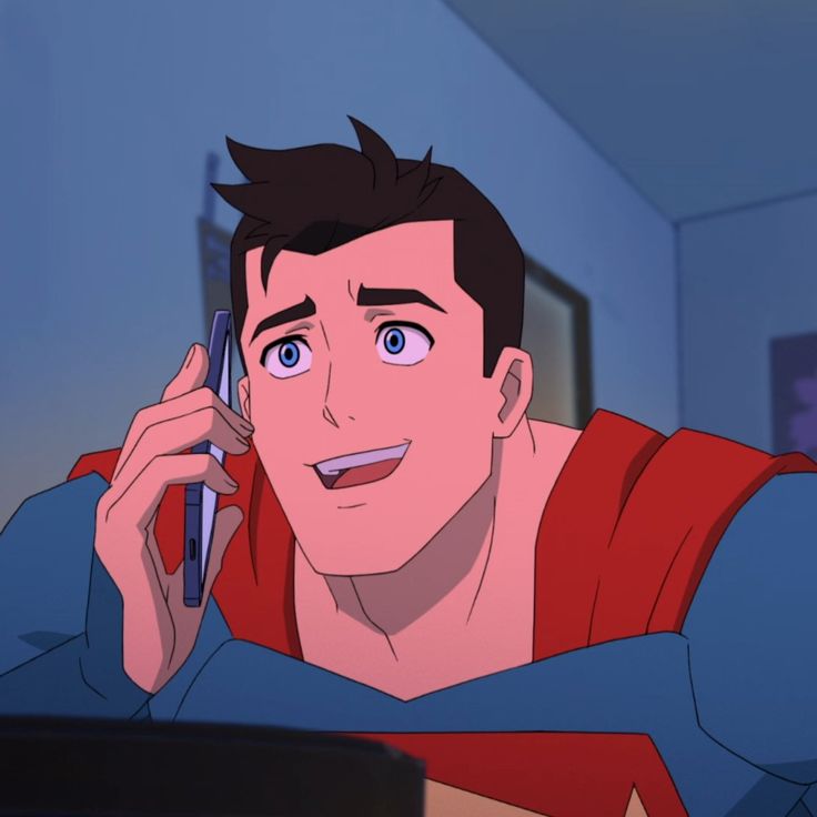 a young man talking on a cell phone while wearing a superman shirt and holding a pen in his hand