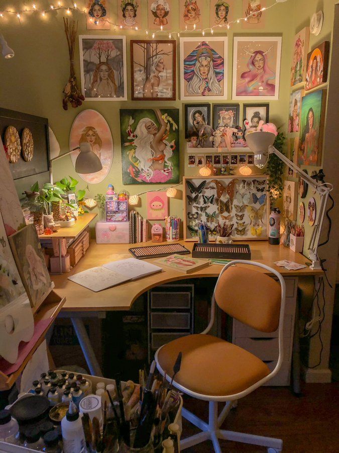 a desk with lots of art on the wall and pictures hanging above it, along with an orange chair