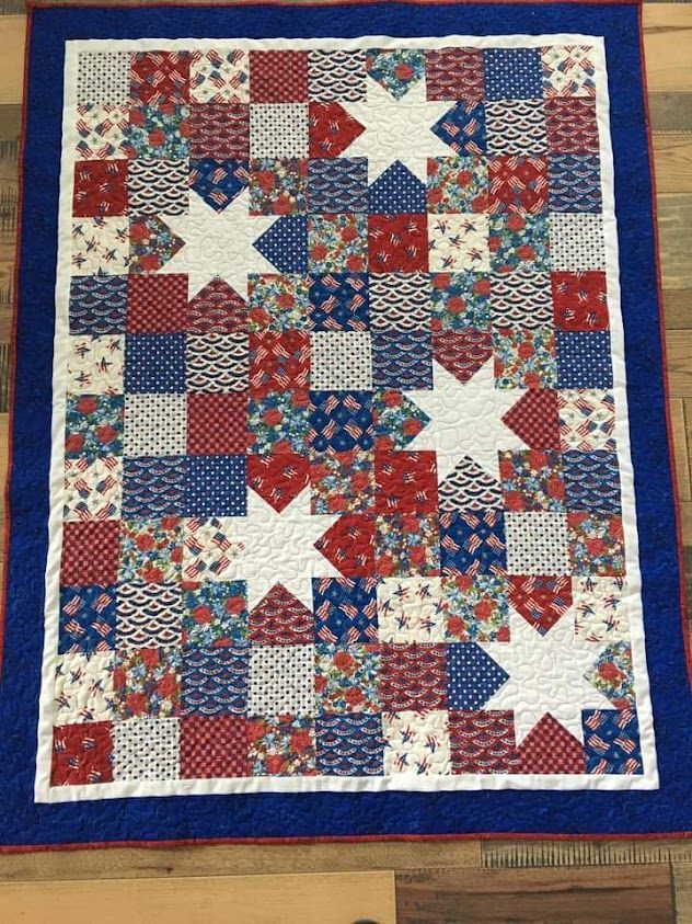 a red, white and blue quilt with stars on it sitting on top of a wooden floor